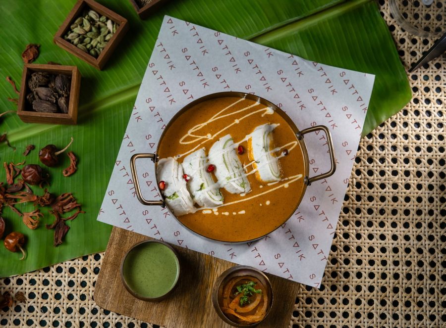 Sliced paneer served on a banana leaf with a copper pot of gravy