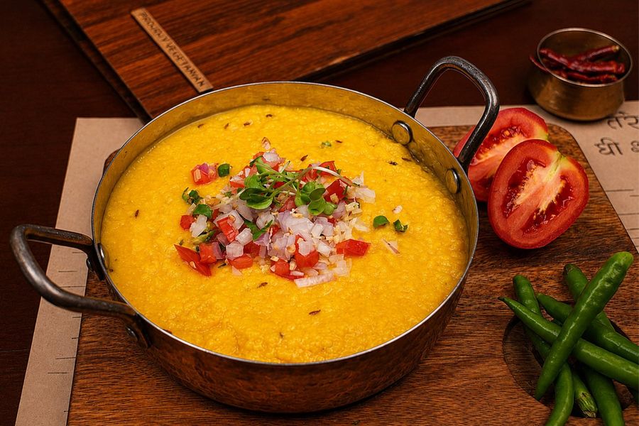 A yellow lentil preparation in a copper kadhai with fresh vegetables
